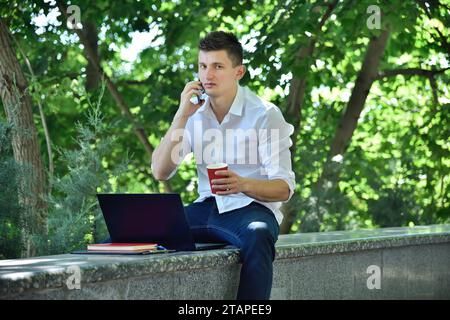 Financial analyst sitting in park and speaks on mobile phone with a colleague. Business and trade concept. Stock Photo