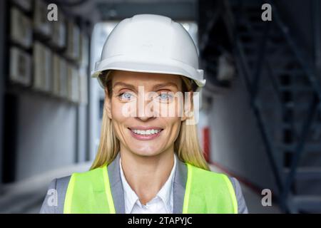 Close-up photo. Portrait of a young smiling female architect, engineer, worker in a safety helmet standing outside a building and looking at the camera. Stock Photo