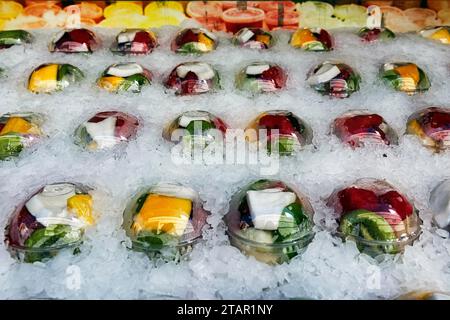 Freshly cut and ready-to-cook fruit in plastic cups, covered with ice, refrigerated counter in supermarket, Spain Stock Photo