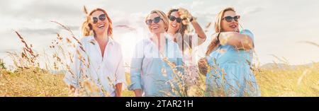 Portrait of four cheerful smiling and laughing women during outdoor walking by a high green grass hill. They looking at the camera. Woman's friendship Stock Photo