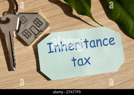 Inheritance Tax. Card, key with key chain in shape of house on wooden table, closeup Stock Photo