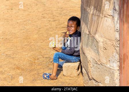 hungry african child eating biscuits , african village homestead yard with shack Stock Photo