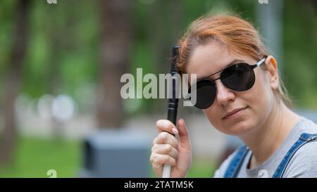 Blind red-haired woman sitting outdoors leaning on a cane.  Stock Photo