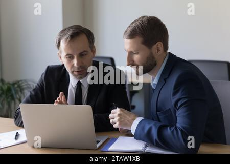 Two serious businessmen working together using laptop in office Stock Photo