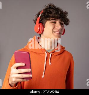Cheerful young man smiling while listening to music on his smartphone with red headphones Stock Photo