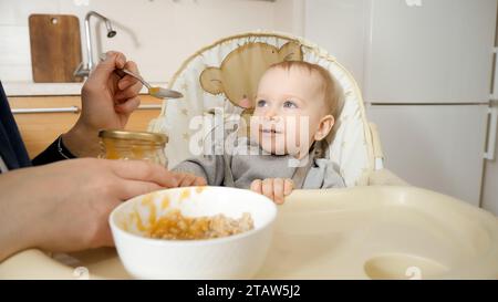 Portrait of little baby boy getting messy while eating porridge in highchair. Concept of parenting, healthy nutrition and baby feeding Stock Photo