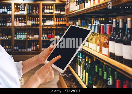 Liquor store manager using digital tablet in front of half of wine bottles. Blank screen of computer tablet and wine shop. Stock Photo