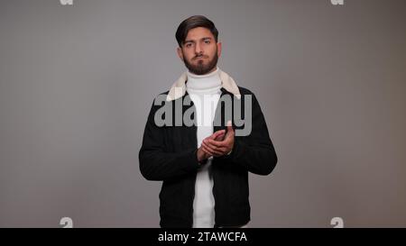 A young man clapping his hands against a gray background. Stock Photo