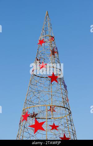 Metal conical Christmas tree with red stars and blue sky background in bury lancashire uk Stock Photo