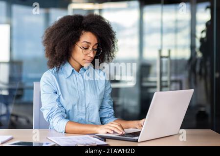 Serious thinking focused woman at workplace inside office working with laptop, business woman typing on keyboard. Stock Photo