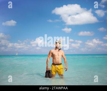 Man in a swimsuit with a diving mask holding snorkeling fins and standing in the sea Stock Photo