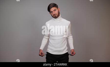 A young man, looking sad, holding an empty packet against a gray background, symbolizing poverty and financial hardship. Stock Photo