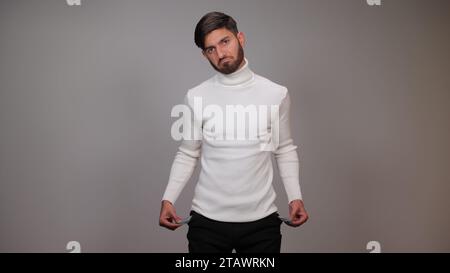 A young man, looking sad, holding an empty packet against a gray background, symbolizing poverty and financial hardship. Stock Photo