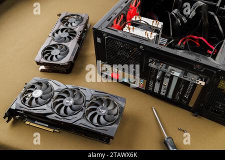 graphics card upgrading concept, two gaming graphics cards near desktop miditower ATX pc case on tan fabric background Stock Photo