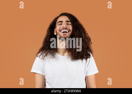 Joyful man with curly brown hair laughs against beige backdrop Stock Photo