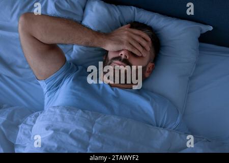 Man Covering Face With Hand Lying Not Sleeping In Bedroom Stock Photo
