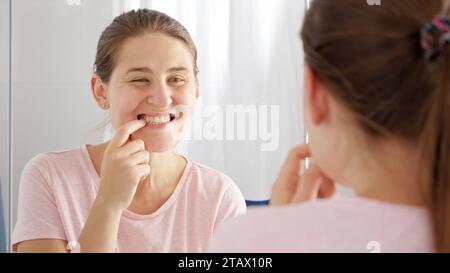 Portrait of smiling young woman looking for plaque and caries on her teeth at bathroom. Concept of teeth health, self checking mouth and oral hygiene Stock Photo