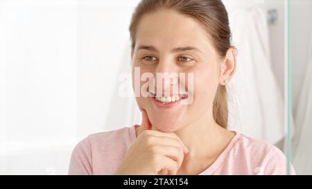Happy smiling woman in pajamas looking in her reflection and checking teeth at morning. Stock Photo