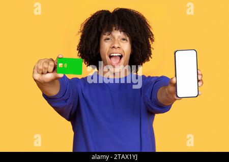 Excited young black man showing credit card and smartphone with blank screen Stock Photo