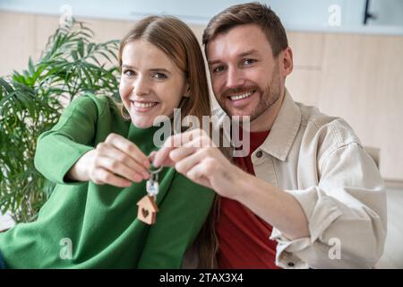 Young spouses bought real estate holding keys in hands smiling looking at camera. Stock Photo