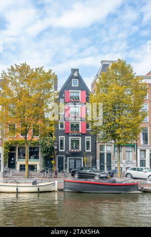 Netherlands. Sunny autumn day in Amsterdam. Facades of typical buildings on the canal embankment. Boats and cars under blue sky with clouds Stock Photo