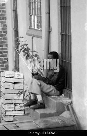 Shop worker taking a break sitting on the back step of shop listening to transistor radio, Johannesburg Gauteng, South Africa, 1985.  From the collection - South Africa 1980s - Don Minnaar photographic archive Stock Photo