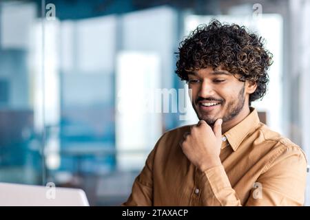 Young successful businessman close up inside office, satisfied man smiling looking at laptop screen, reading email message at workplace. Stock Photo