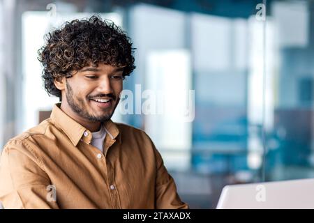 Young successful businessman close up inside office, satisfied man smiling looking at laptop screen, reading email message at workplace. Stock Photo