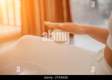 Athletic slim caucasian woman doing thigh self-massage with a massage ball indoors. Self-isolating massage Stock Photo