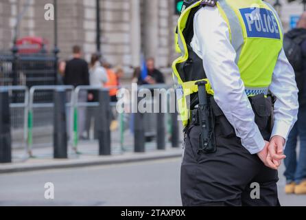 Metropolitan Police officer wearing a high visibility vest, escorting and monitoring a street protest demonstration near Downing Street, London, UK. Stock Photo
