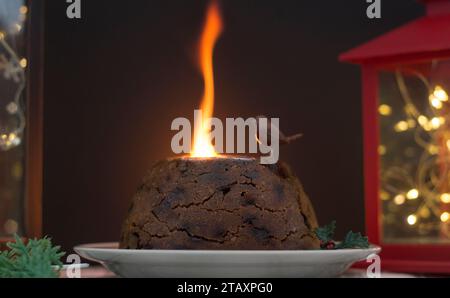 Flaming traditional Christmas pudding with brandy on top watched by an inquisitive ornamental robin Stock Photo