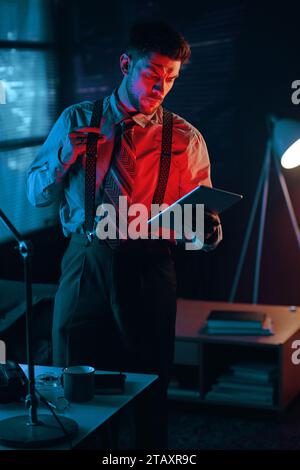 Young serious male analyst or director of business company with tablet looking through data in electronic document in dark office Stock Photo
