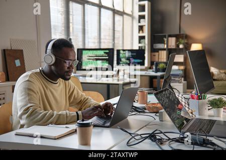 Software developer listening to music in headphone when coding on laptop in office of IT company Stock Photo