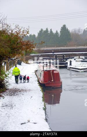 Person walking dogs along the towpath past narrowboat moored on the Trent and Mersey canal in the snow in winter at Wheelock locks Cheshire England UK Stock Photo
