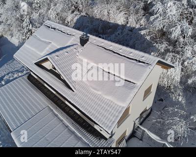 Snow blankets solar panels on a house roof in winter. Despite the chilly surroundings, the photovoltaic panels stand resilient. Perfect for illustrati Stock Photo