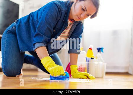 A young woman in protective gloves washes the floor with a brush and detergent Stock Photo