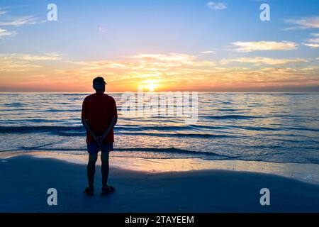 A senior man alone on the beach at sunset. Concept of solo travel, loneliness and isolation. Stock Photo