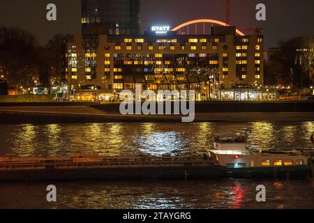 Das Hyatt Regency Hotel am Rhein, in Köln Deutz, dahinter der beleuchtete Bogen der Lanxess Arena, Frachtschiff auf dem Rhein, NRW, Deutschland Hyatt Hotel Köln *** The Hyatt Regency Hotel on the Rhine, in Cologne Deutz, behind it the illuminated arch of the Lanxess Arena, cargo ship on the Rhine, NRW, Germany Hyatt Hotel Cologne Credit: Imago/Alamy Live News Stock Photo