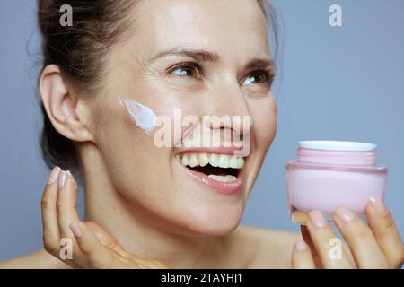 happy modern middle aged woman with cosmetic cream jar isolated on blue. Stock Photo