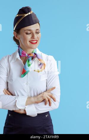 happy stylish female flight attendant against blue background in uniform looking at copy space. Stock Photo