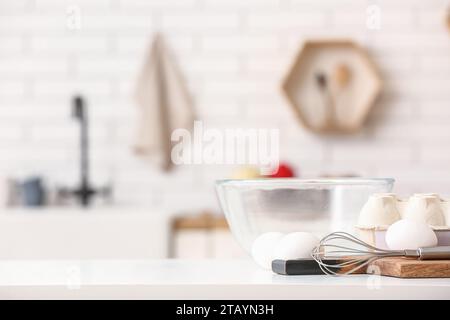 Package with eggs, whisk and glass bowl on table in kitchen Stock Photo