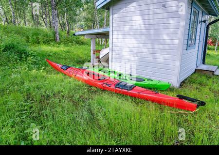 Two kayaks - red and green ones are on the green beside the shed. Summer vacation in mountains, Sweden, Lapland Stock Photo