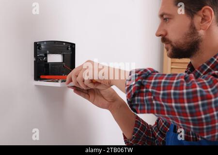 Technician installing home security alarm system on white wall indoors Stock Photo
