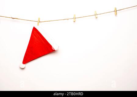 Santa hat with clothespins hangs on a rope against isolated white background Stock Photo