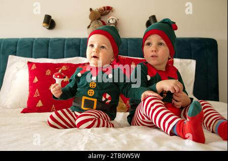 Baby girl and toddler dressed as elves sitting on a bed Stock Photo