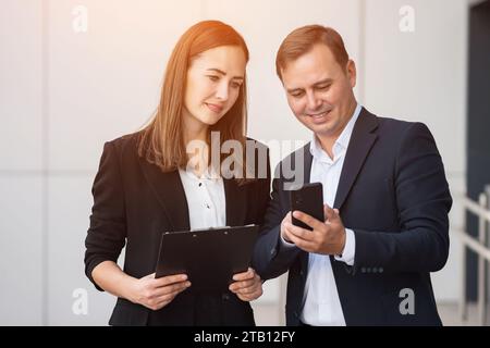 Man and woman smile reading text message from top manager on phone Stock Photo