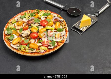 Homemade pizza and various ingredients. Grated cheese on paper. Cheese grater. Pizza cutter. View from above. Black background Stock Photo