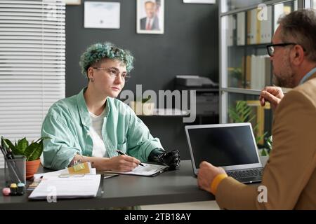 Young woman with disability filing documents and talking to advisor during meeting in office Stock Photo