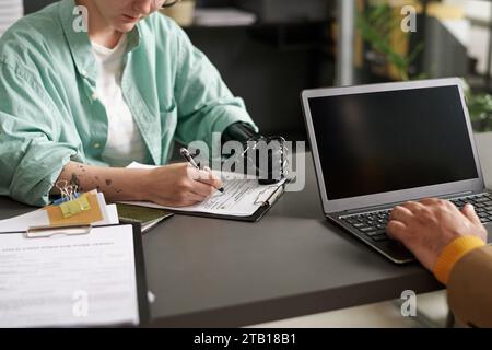 Young woman with disability filing document while having meeting with consultant in office Stock Photo
