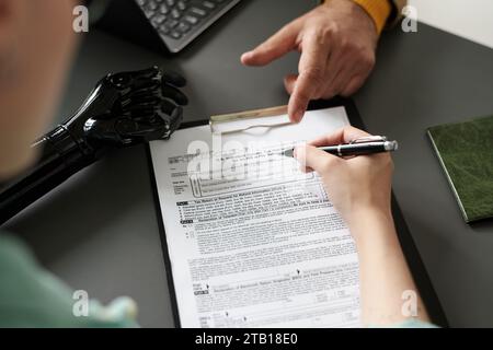 High angle view of woman with disability filing insurance documents during meeting with consultant in office Stock Photo
